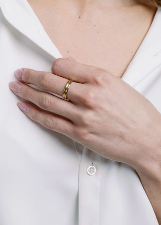Hand wearing a gold and silver ring on a white shirt background