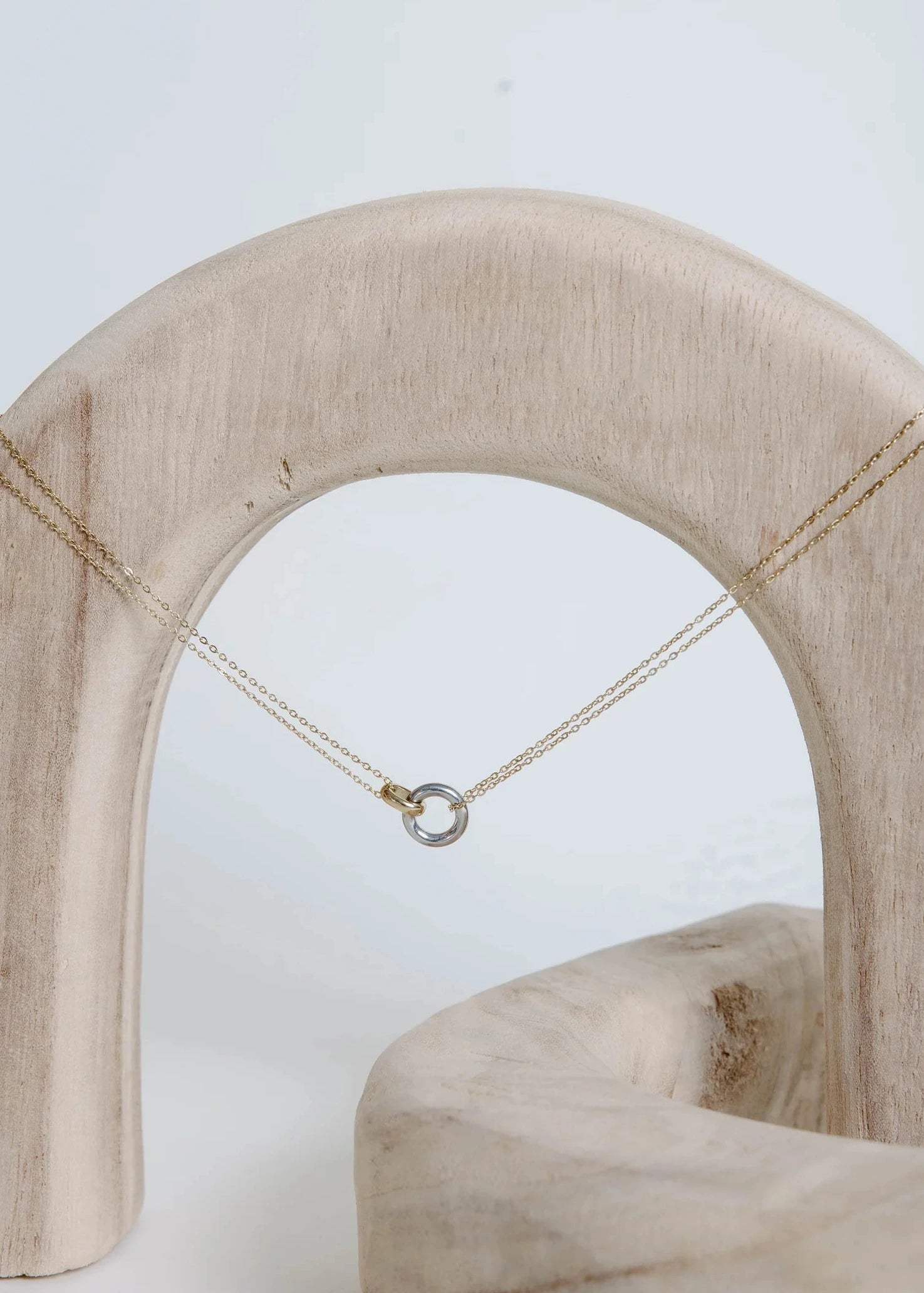 Gold and silver necklace on a wooden arch with a white background