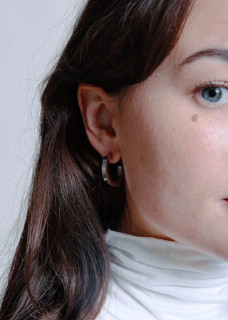 Close-up of a person wearing hoop earrings with a neutral background