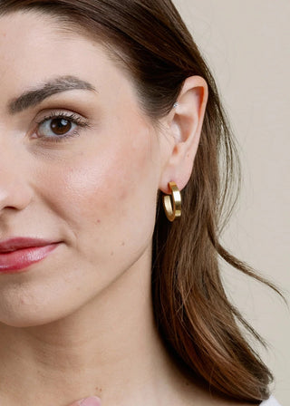 Woman wearing gold hoop earrings with a neutral background
