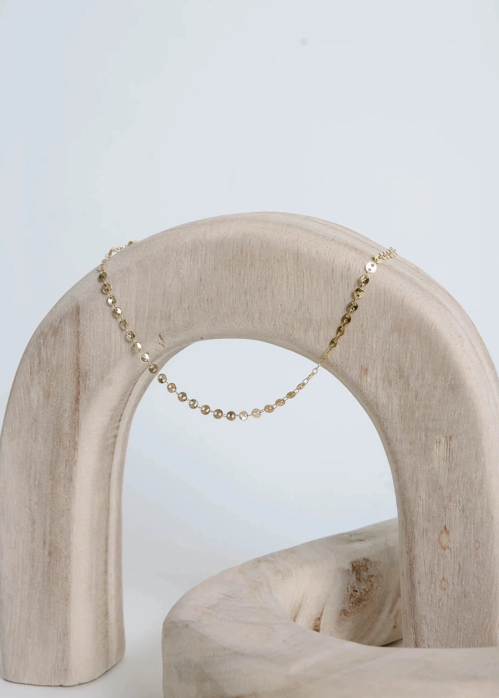 Gold necklace on a wooden arch with a light blue background