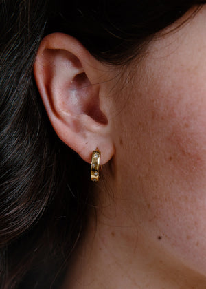 Close-up of an ear wearing a gold hoop earring with dark hair and skin visible.