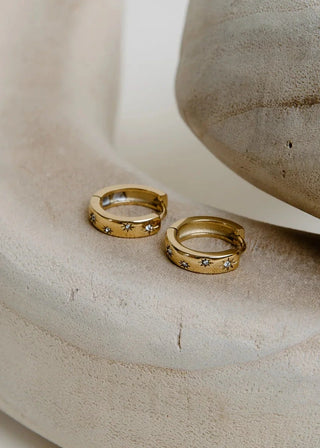 Two gold earrings on a curved stone surface with a plain background